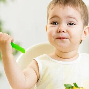 Otrok drži žlico in je hrano.