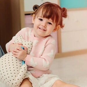 Nasmejan malček sedi na tleh in se igra.