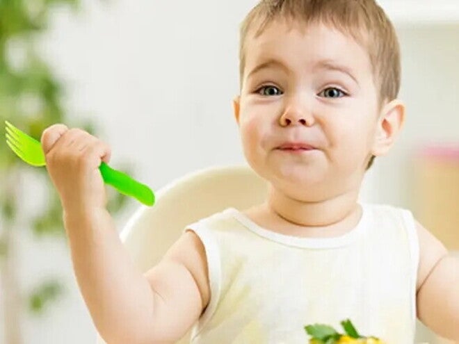 Otrok drži žlico in je hrano.