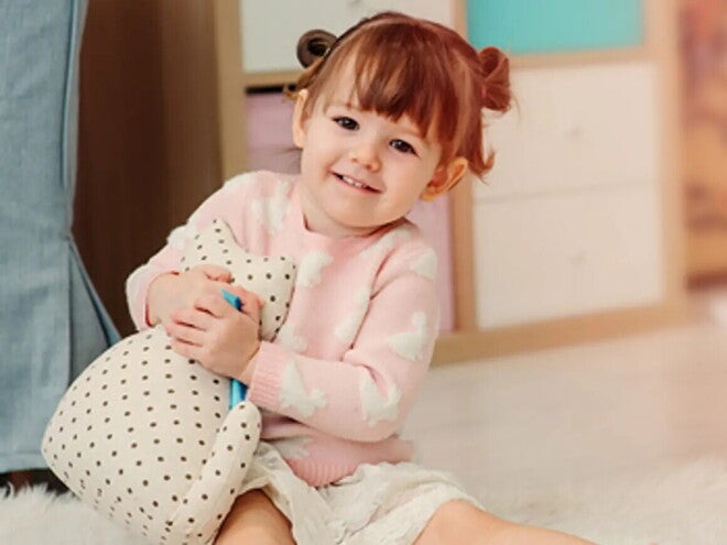 Nasmejan malček sedi na tleh in se igra.