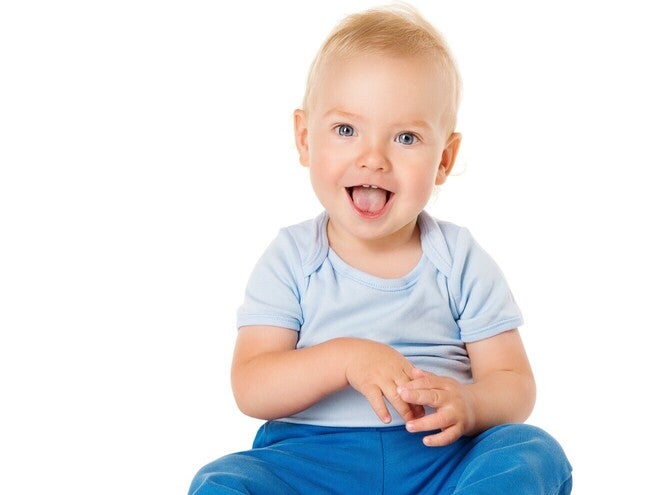 Dojenček v modrih oblačilih sedi na beli podlagi.