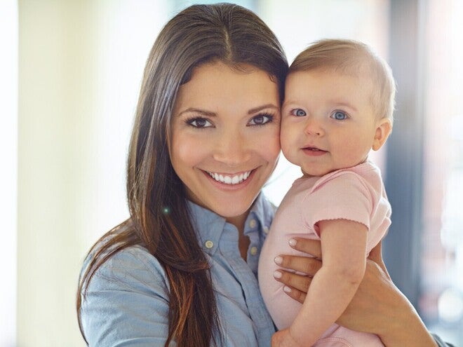 Ženska drži otroka v svetlem prostoru, oba sta obrnjena proti kameri.