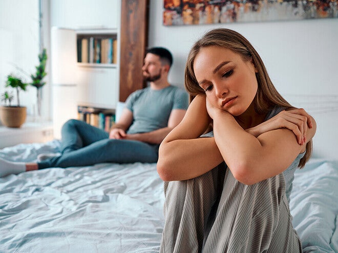 Photograph: couple on bed, woman looking sad in foreground, man turned away