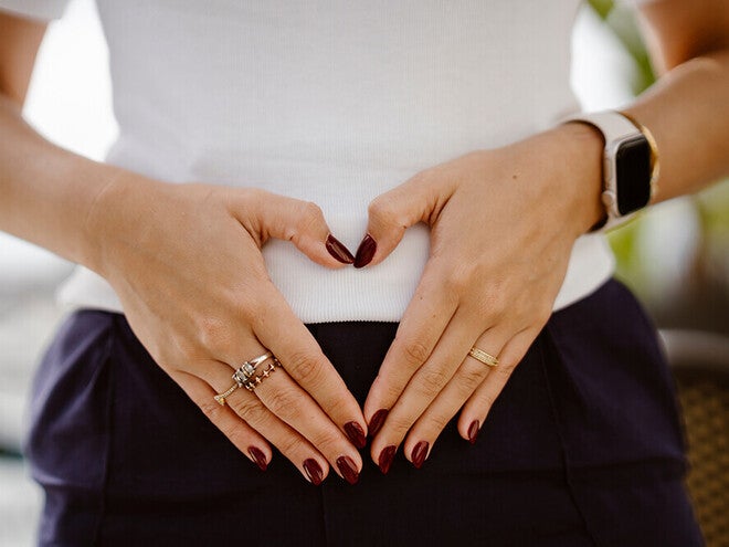 Photograph of hands forming a heart over lower abdomen, red nails and a smartwatch