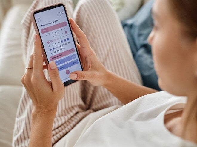 Ženska gleda koledar na pametnem telefonu, sedi na kavču.