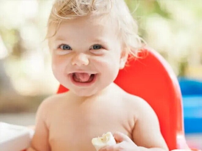 Nasmejan dojenček sedi na stolu.