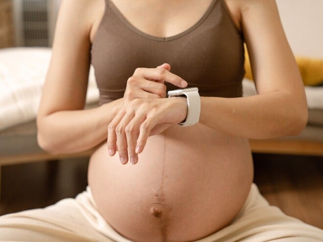 Nosečnica v rjavem nedrčku preverja pametno uro na zapestju.